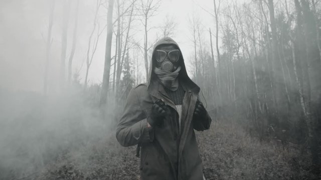 Human wanderer in gas mask and military clothes walking on old railway in clouds of toxic smoke. Male survivor stalker after nuclear or chemical war in empty dead forest. Post apocalyptic world