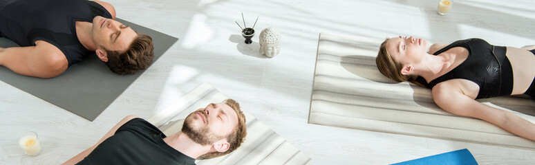 panoramic shot of young people meditating in corpse pose near decorative buddha head, aromatic...