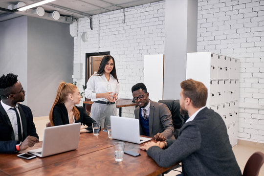 Young and beautiful caucasian and african people in formalwear sit together on table using laptop and discussing issues on the agenda