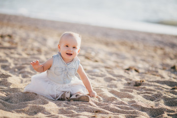 Happy baby girl sitting on sand near sea at beach.