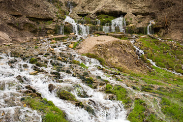 Natural textures. The spring flows from a steep rocky hillside. Early spring. Izborsk, Pskov region, Russia.