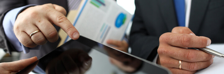 Focus on businessman hand pointing to empty screen of tablet. Businesspeople discussing conditions...