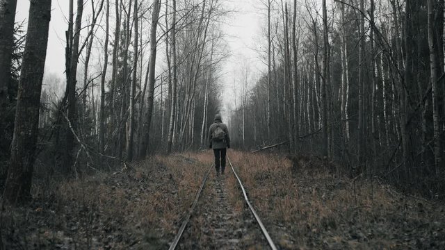 Wanderer man in military clothes walking on old abandoned railway in empty dead forest. Apocalypse concept, male stalker survivor after nuclear or chemical disaster. Post apocalyptic world concept