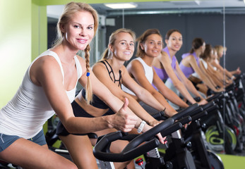 Fototapeta na wymiar Portrait of women on exercise bike gesturing thumbs up at gym