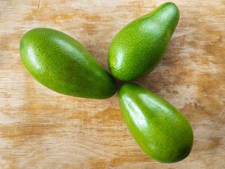 Top view on three avocado lying on a wooden cut board 