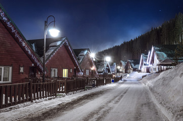 Fototapeta premium row of wooden houses on a snow-covered street in winter at night with dark sky