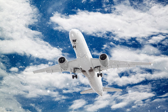 white passenger plane has released its landing gear and is landing through falling snow against background of beautiful white clouds on blue sky