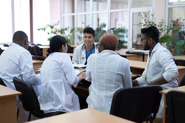 group of young doctors, mixed race, sitting at the table in the hospital, discussing medicine