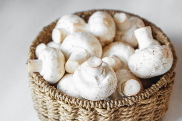 Mushrooms champignons in a round wicker basket on a white wooden table. Close up. Place for text or advertising