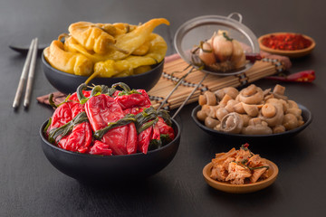 Fermented products red and green hot peppers, mushrooms on a black table - traditional Korean food. Copy space