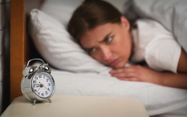 Young Woman Looking At Clock Lying In Bed At Home
