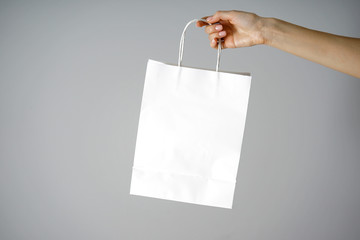 Black friday concept. Paper white craft bag, eco packaging in a female hand, on a gray background. Place for text.