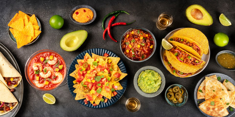 A panorama of Mexican food, many dishes of the cuisine of Mexico, flat lay, overhead shot on a black background. Nachos, guacamole, shrimp cocktail, tacos...