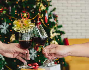 Close up people cheers and clinking red wine glass for celebrate holiday event party in christmas tree background