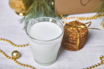 Christmas glass with milk and cookies For Santa on the table with Christmas Tree, gifts, decorations on white wooden background. Letter for Santa.