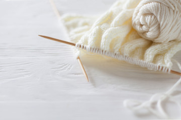 Knitting needles, white yarn, wooden background.