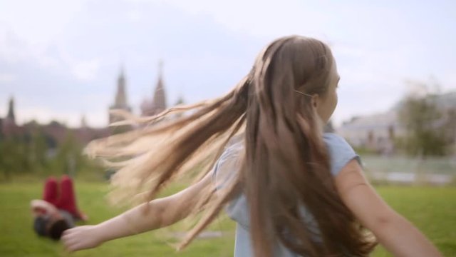 Charming long-haired 10 years old girl in a blue dress circling in the dance in a city park in the summer. Slow motion, close-up. Moscow Kremlin in defocus on the background. cloudy day