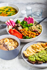 Vegan lunch. Chocolate smoothie bowl, Buddha bowl with tofu, chickpeas and quinoa, lentil soup and toasts on a gray background.