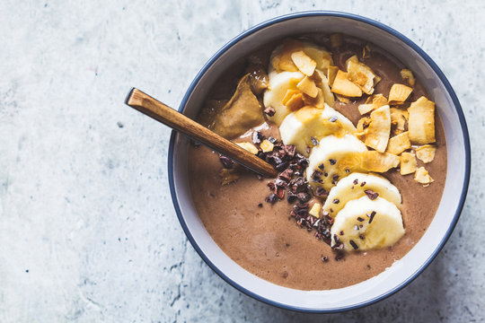 Chocolate smoothie bowl with banana, coconut and chocolate in a gray bowl, top view.