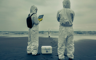 Unrecognizable people with bacteriological protection suits looking for evidence at sea