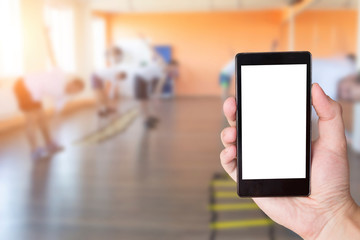 Hand with mobile phone in the background of people engaged in a fitness center. Gym and fitness phone app concept, copy space