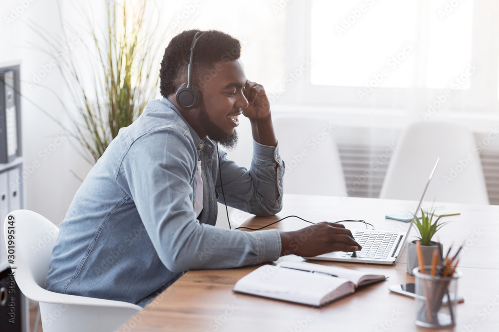 Poster cheerful manager wearing headset and using laptop, speaking with client
