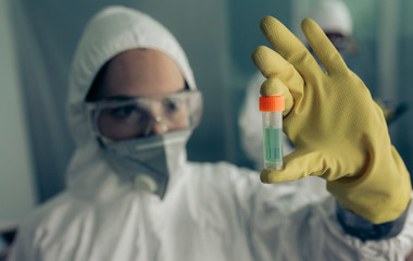 Female doctor with baceriological protective suit looking at an antidote vial for a dangerous virus - obrazy, fototapety, plakaty