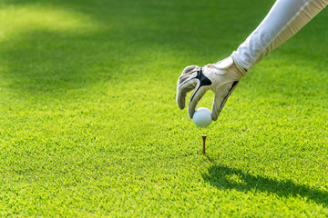 Close up hand asian sporty woman putting golf ball on tee with club in golf course on evening on time for healthy sport. Banner and copy space for text.  Lifestyle and Sport Concept