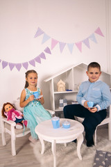 cute little boy and girl sitting on the table and drinking tea
