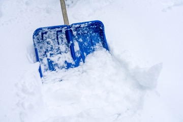 Blue snow shovel/spade outdoors removing the deep snow during snowy weather. Climate and season...
