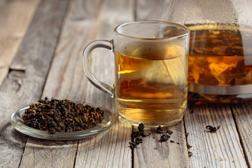Hot green tea in glass mug. Dried tea leaves and hot drink on a wooden table.