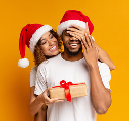 Black millennial couple with Christmas gift on orange background