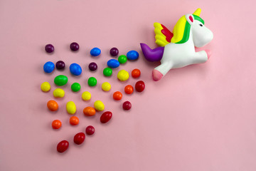 squishy toy unicorn is flying on a candies rainbow on pink background top view flat lay