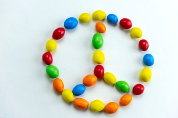 Fototapeta na wymiar peace sign made from bright multicolored candies top view flat lay on a white background