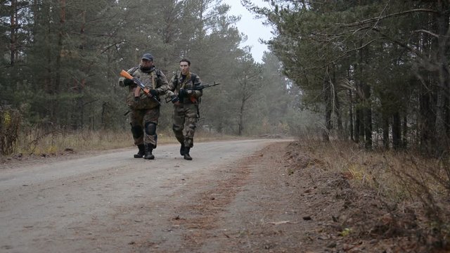 two men armed with Kalashnikovs mashine guns walk along a forest road