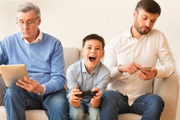 Boy Playing Videogame Sitting Between Grandfather And Father At Home