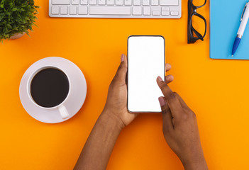 Black female using smartphone and drinking coffee at workplace