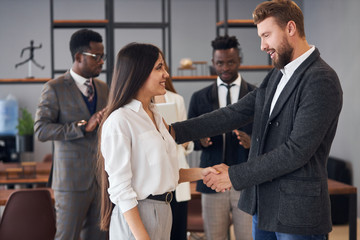 Side view on caucasian people shaking hands. Beautiful woman with long black hair in meeting with caucasian leader of company, man in tuxedo shake hand to her