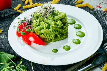 Vegetarian pesto pasta with microgreen. Pasta with green sauce and tomatoes on a white plate and gray cloth. Healthy and balanced food. Close up view.