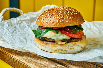 Juicy burger with melted cheese with a meat patty on craft paper. Yellow background. Street, fast food. Close up. Copy space.