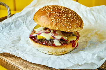 Juicy burger with melted cheese with a meat patty on craft paper. Yellow background. Street, fast food. Close up. Copy space.
