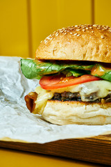 Juicy burger with melted cheese with a meat patty on craft paper. Yellow background. Street, fast food. Close up. Copy space.