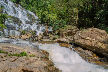 long exposure shot scenery view of waterfall in the lush green forest during day time with strong sunlight