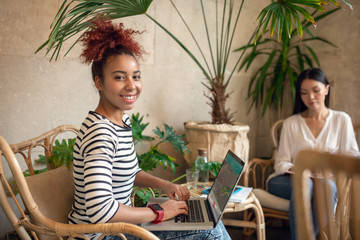 Fototapeta na wymiar Curly businesswoman using laptop while sitting near friend