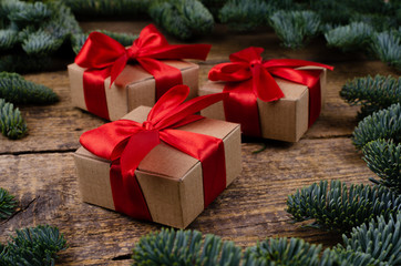 Fototapeta na wymiar Close view of three gift boxes with red bows around which there are branches of fir on a wooden textured background.