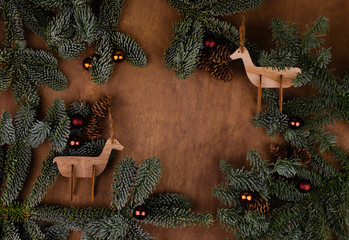 Two wooden deer toys on a brown background surrounded by live branches of spruce and Christmas...