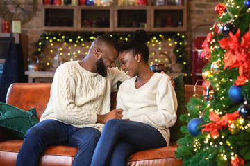 Romantic afro couple sitting on sofa near Christmas tree