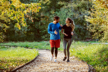 Full length of cute caucasian couple in sportswear walking on trail in woods, smiling and talking