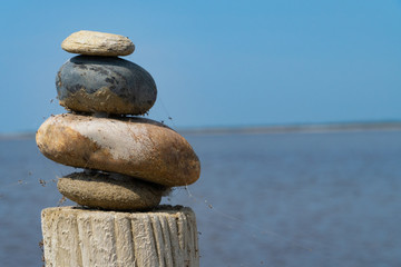 Fototapeta na wymiar A stack of colorful stones on a wooden column in front of the sea and the blue sky