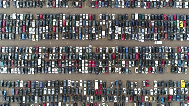 Aerial top down view moving over automaker car distribution lot with vehicles parked close to each other in straight lines waiting for further transportation to resellers and dealers 4k quality